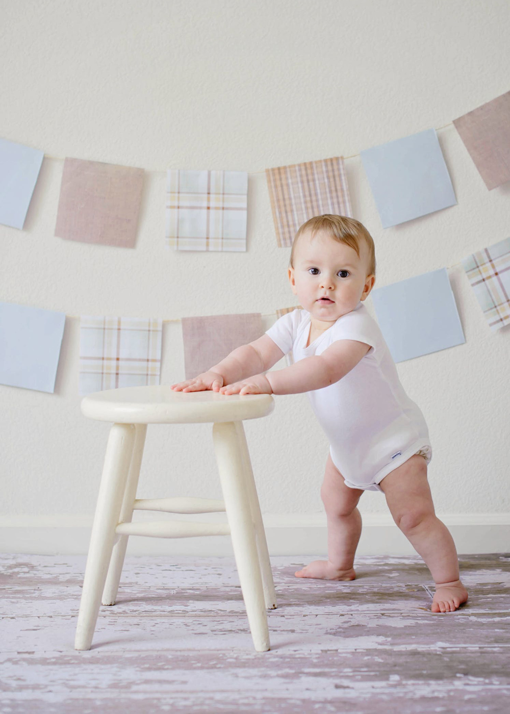 Baby propping himself up with painted white stool and bunting in the background