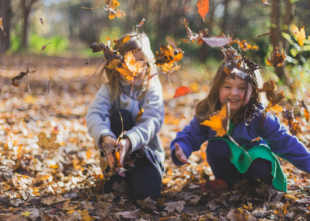 Two young girls trowing leaves in the woods