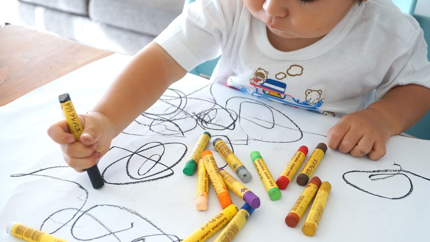 Child drawing with colourful crayons on paper