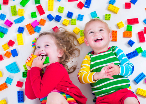 Young children lying down laughing and playing with lego bricks