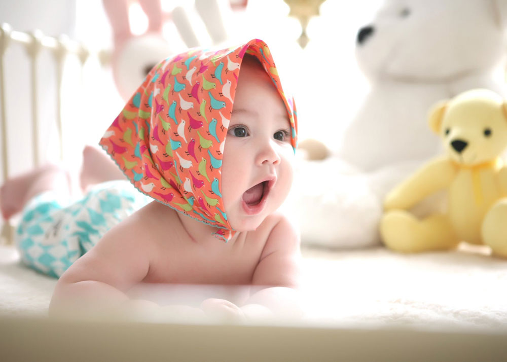 Baby yawning in cot with a orange head scarf