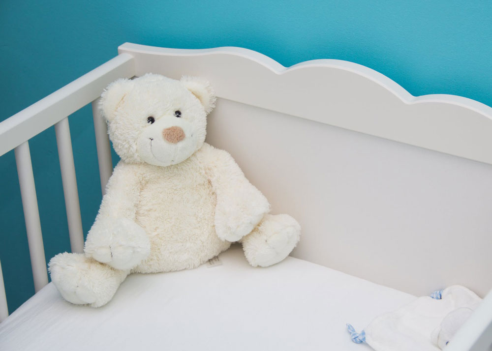 White teddy bear in cot with blue painted walls