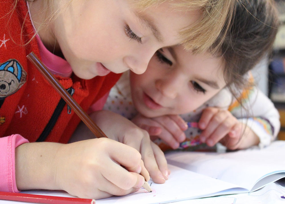 Two young girls drawing in colouring book