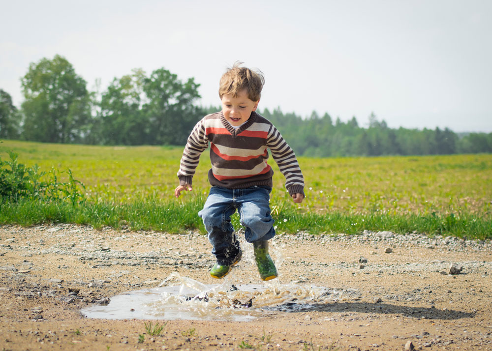 Boy jumping and splashing in puddle